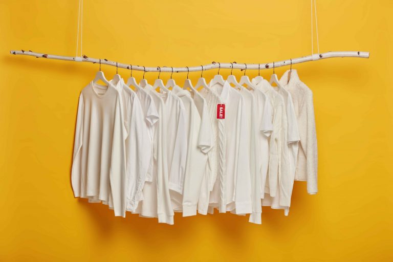 fashionable white clothing hangers with red tag inscriped sale hanging wooden rack against yellow background copy space scaled